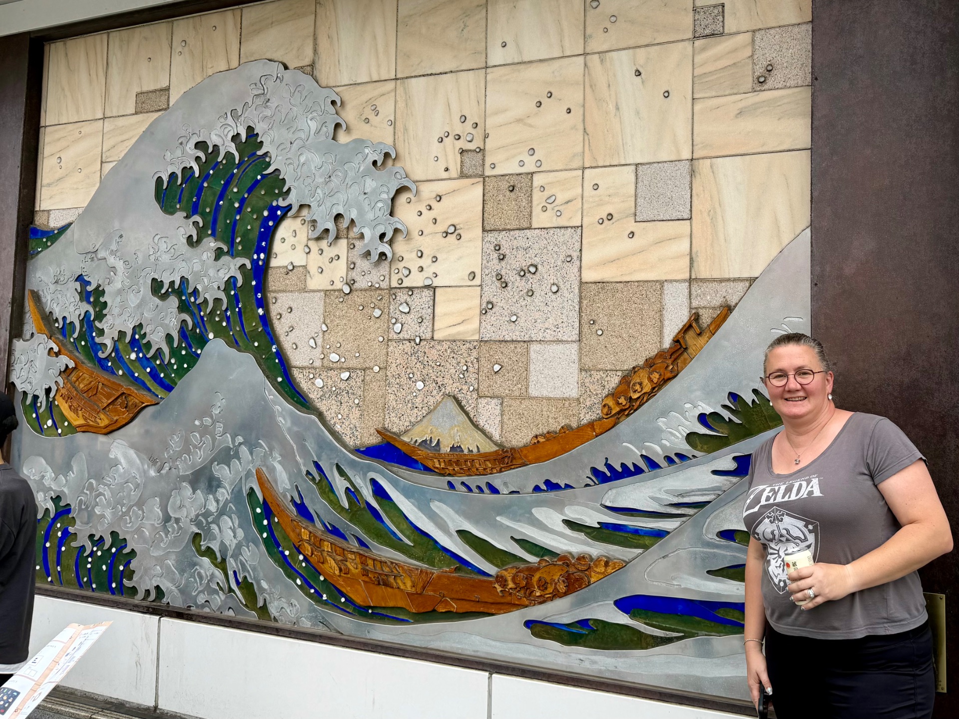 Woman posing next to large decorative wave artwork featuring blue and green water and gold accents on ship interior wall.