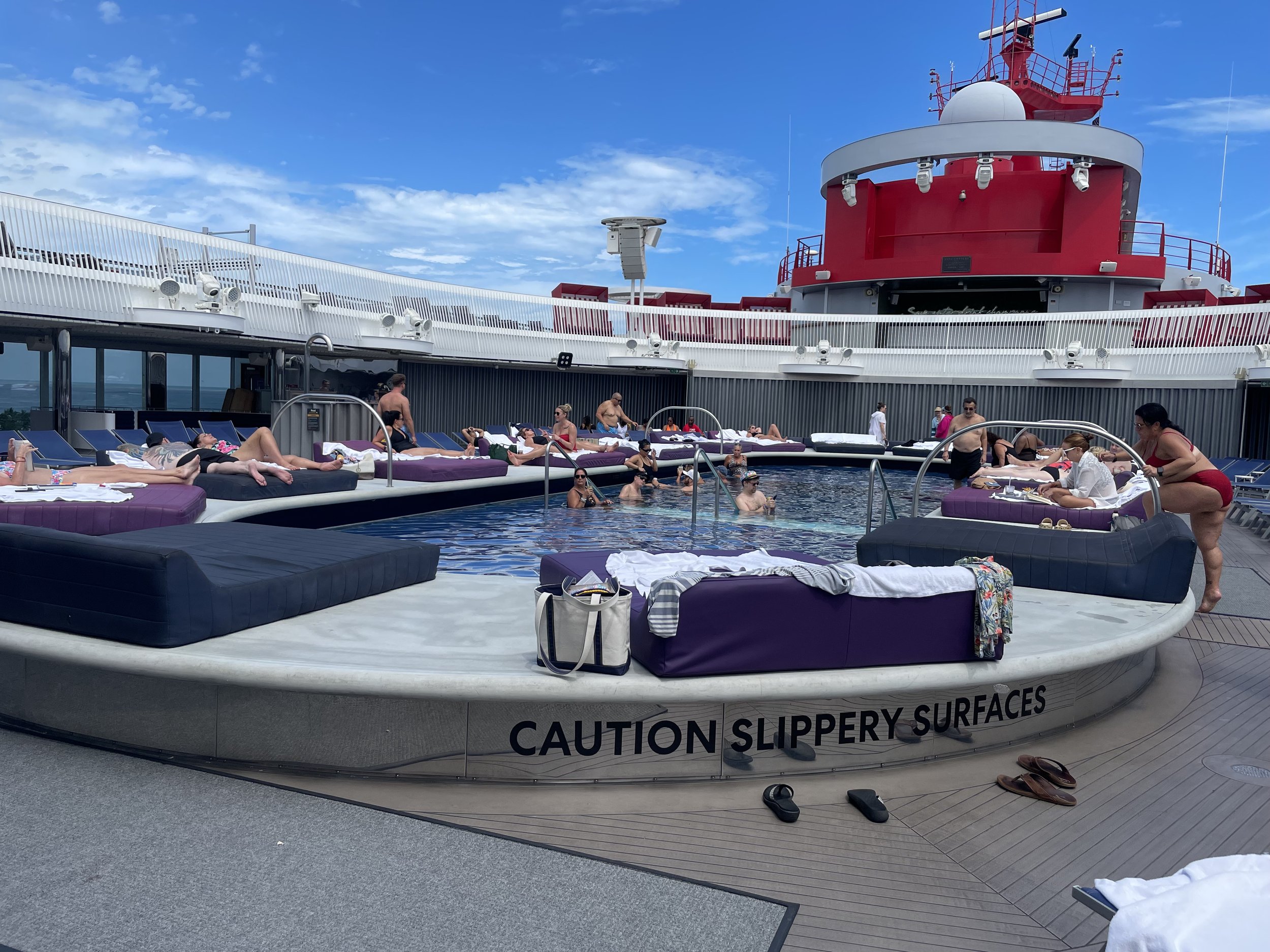 Passengers relax by pool deck on cruise ship with red funnel