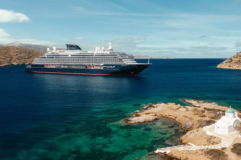 Large cruise ship anchored in Mediterranean island cove with white chapel