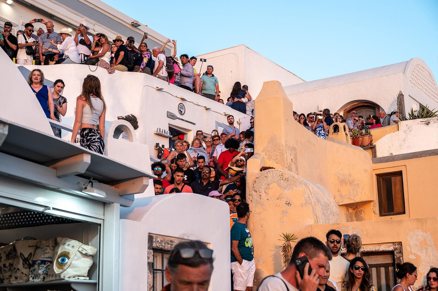 Large cruise ship docked at Mediterranean island with tourists crowded on terraced buildings