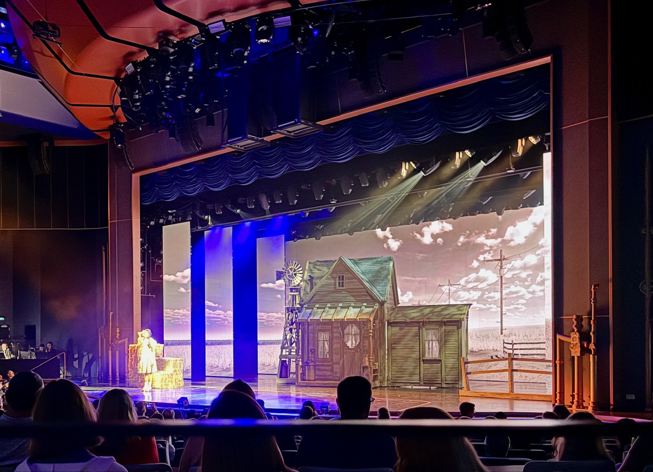 Theater stage production with farmhouse set and prairie backdrop