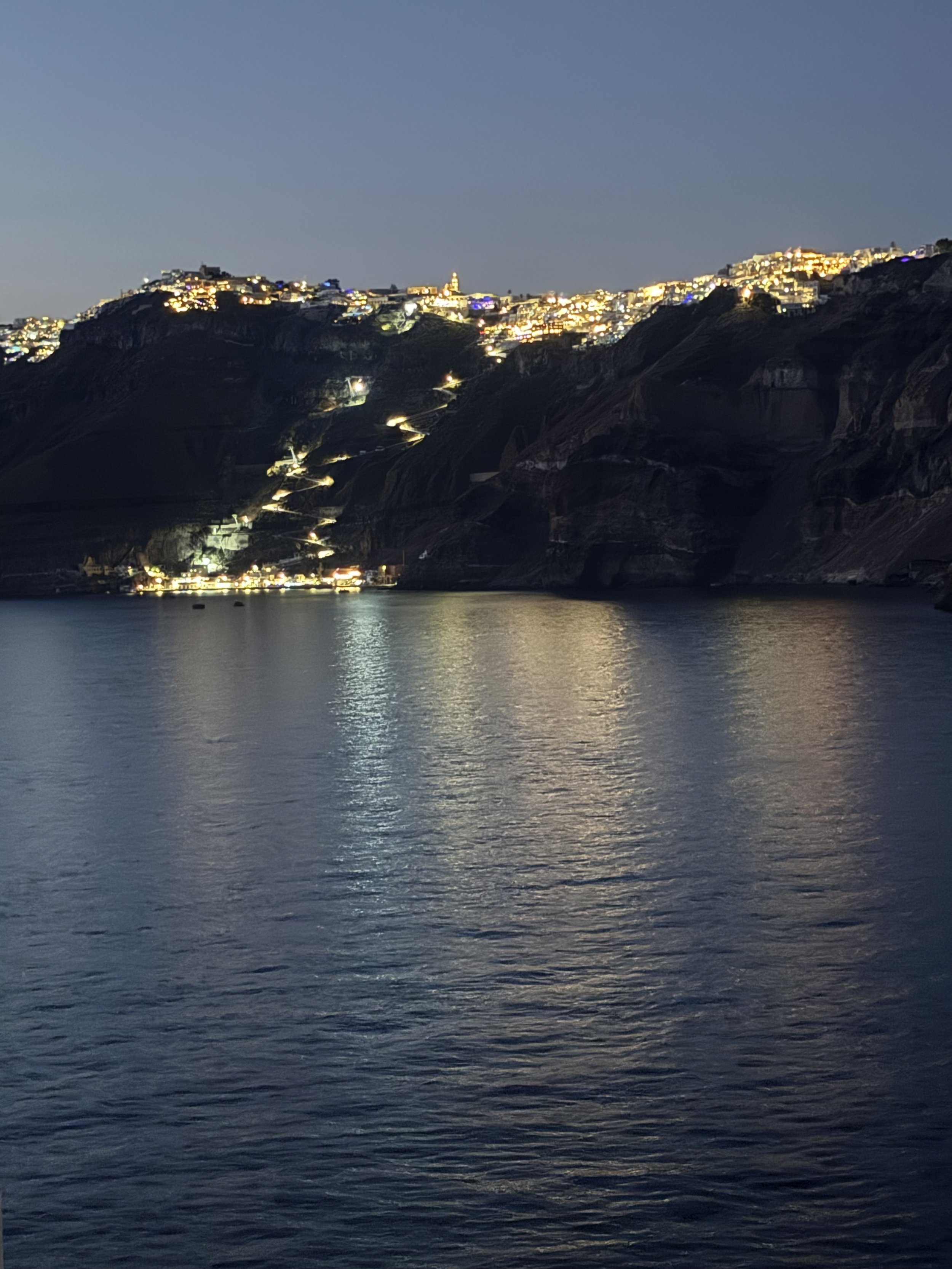 Evening view of illuminated cliffside town reflecting in calm water