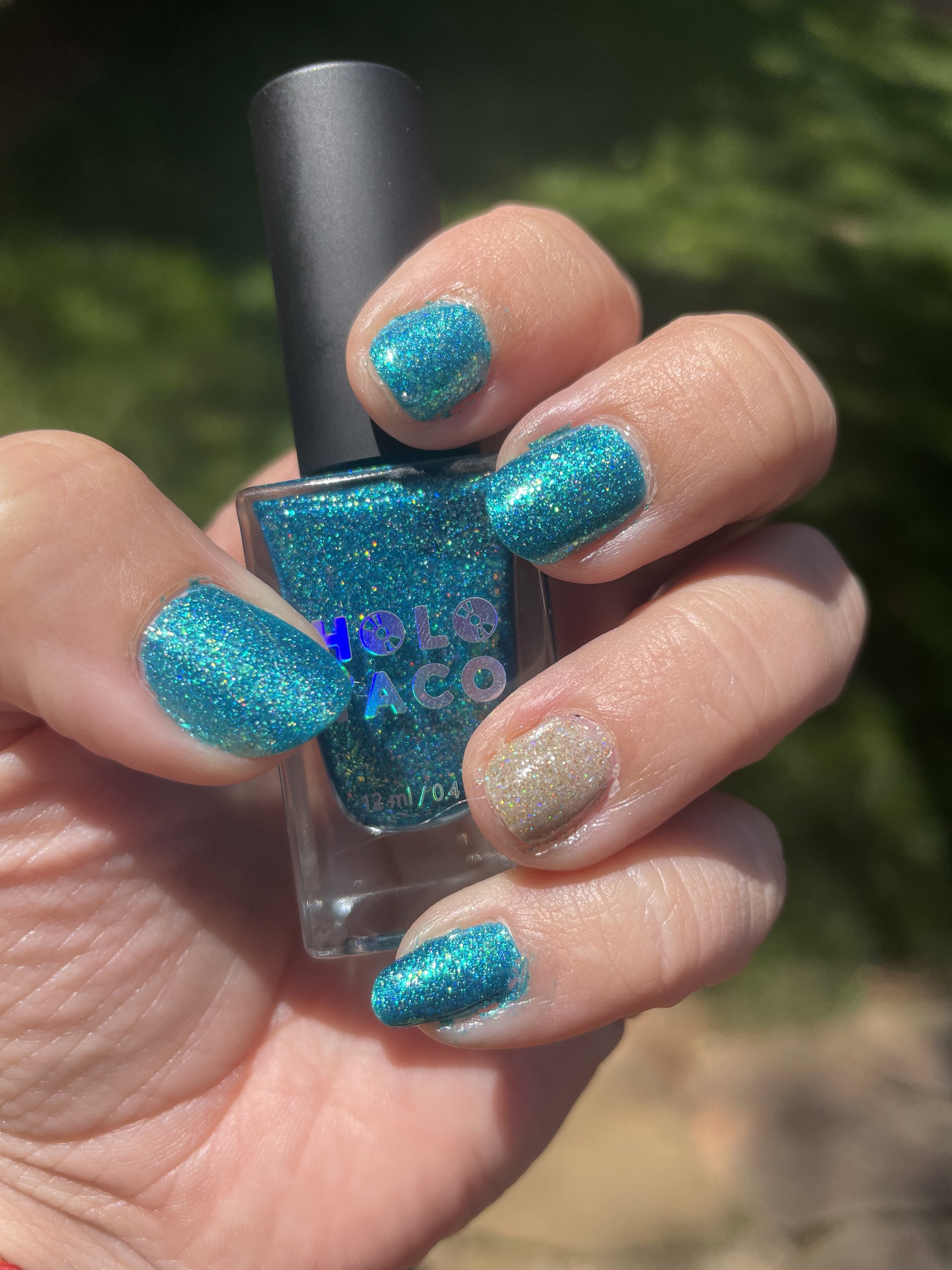 Turquoise glitter nail polish manicure with accent nail displayed outdoors