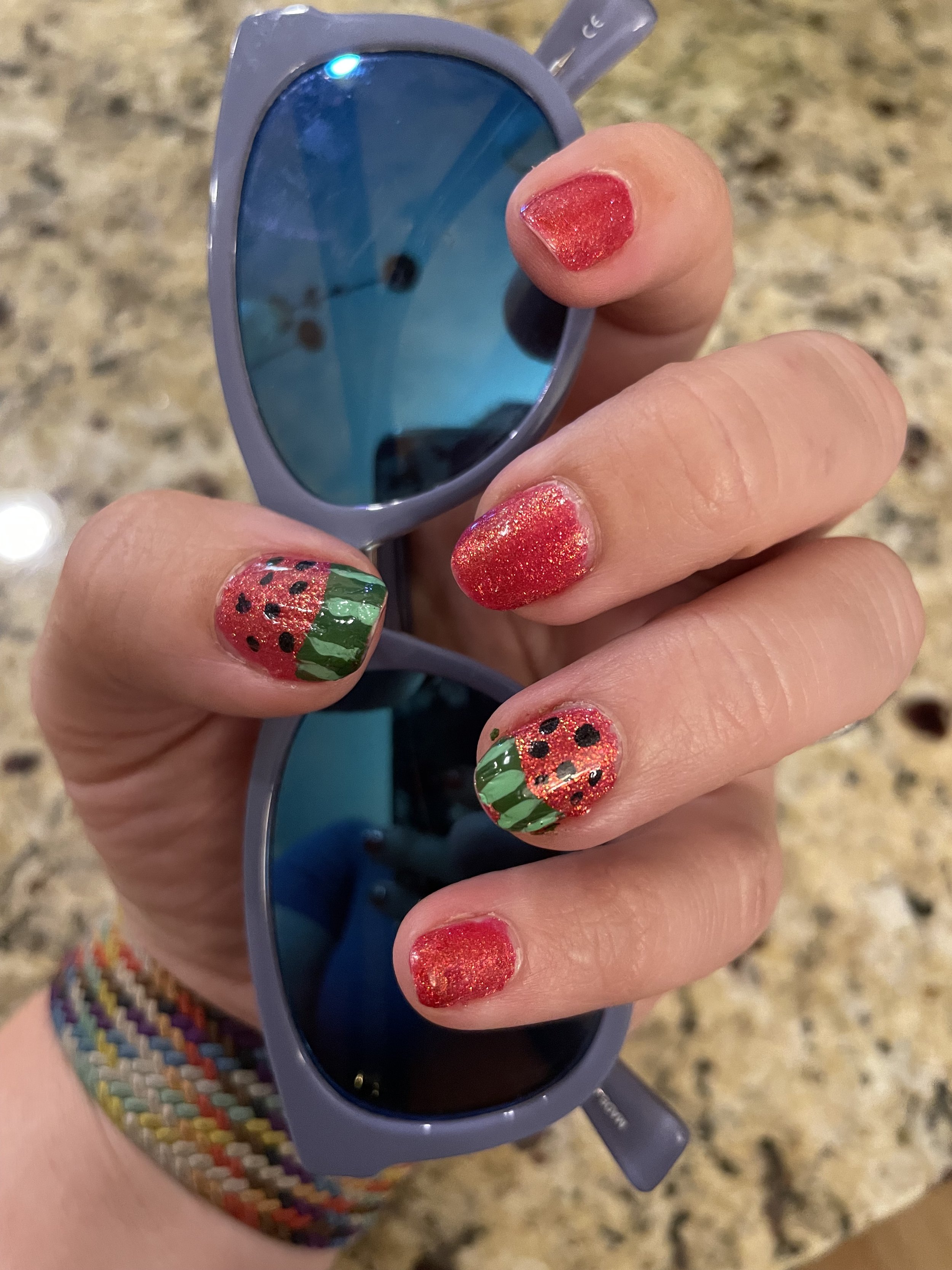 Woman displaying strawberry-themed nail art holding sunglasses
