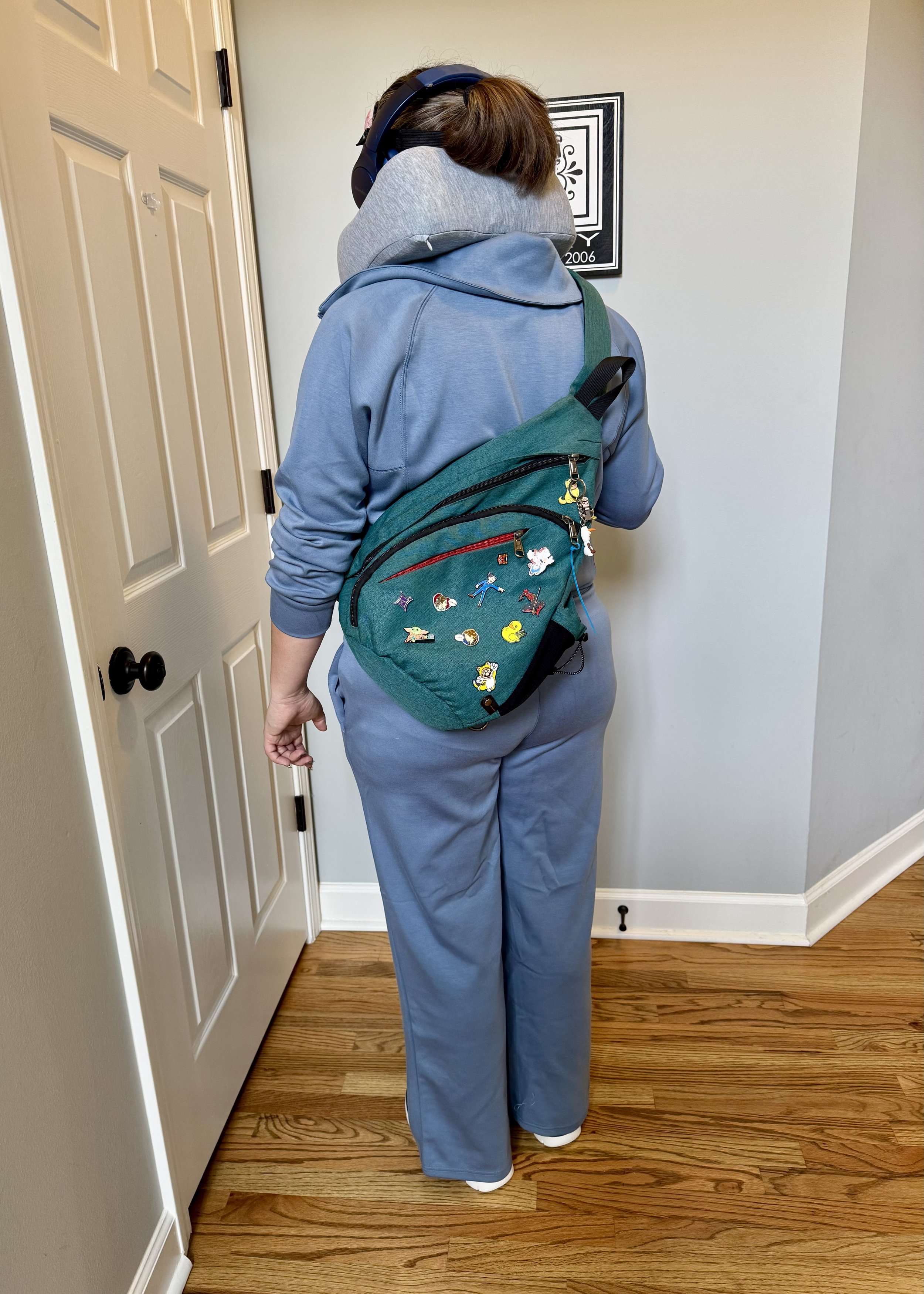 Person wearing blue jacket and green backpack decorated with pins standing in hallway