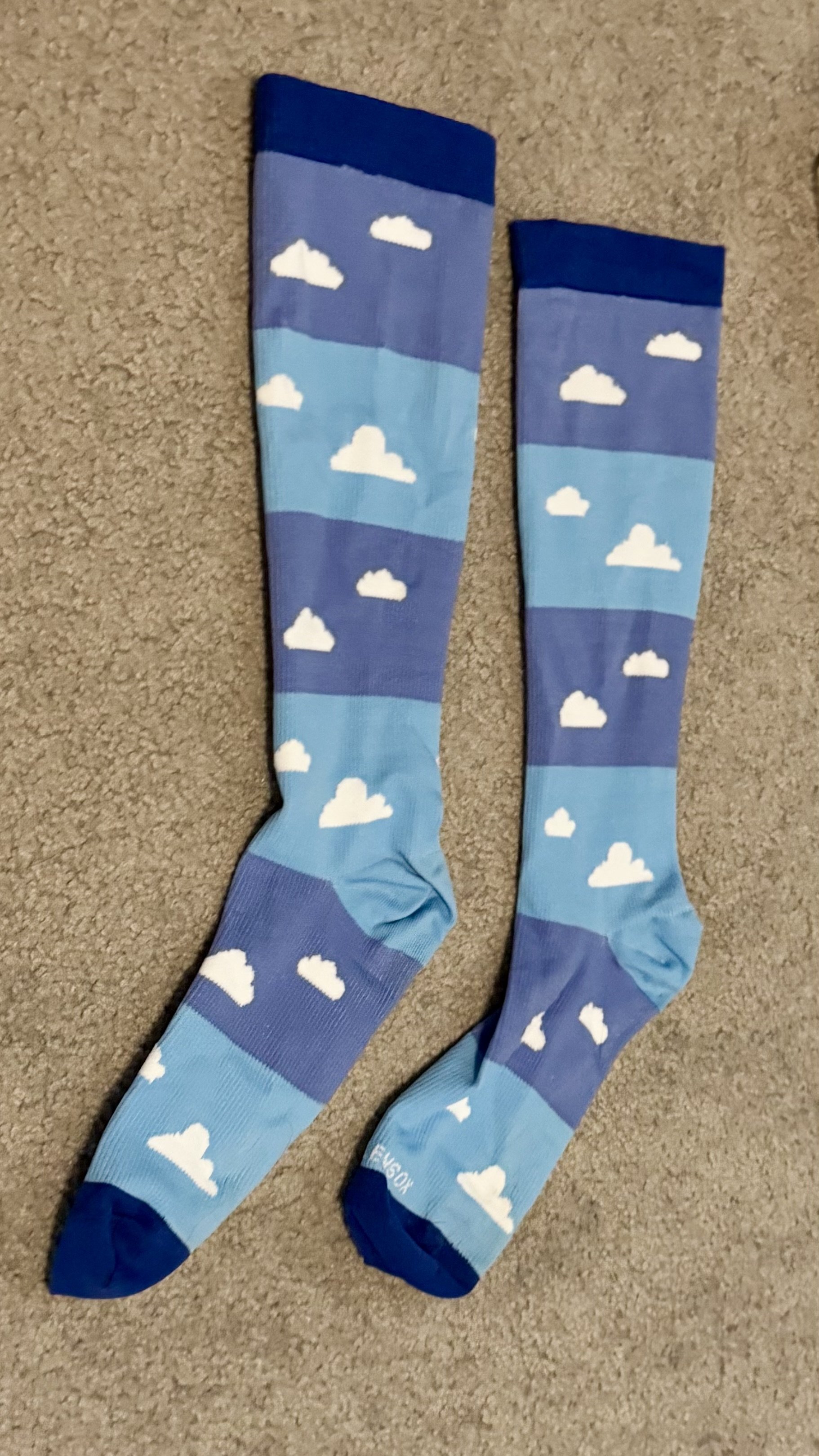 Pair of knee-high socks with sky-themed design featuring white clouds on alternating navy and light blue horizontal stripes.