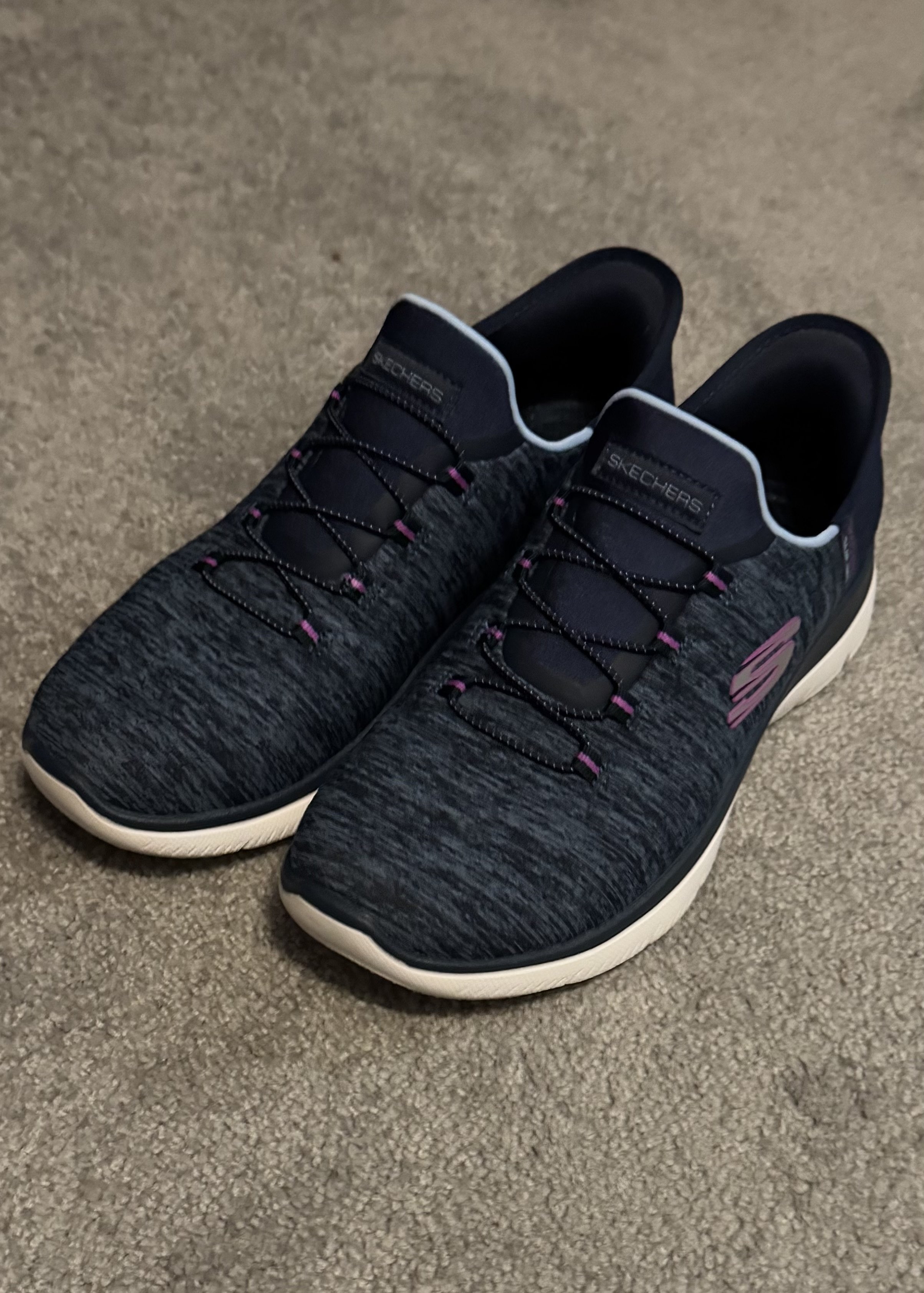 Pair of black and purple Skechers slip-on sneakers with white sole on gray carpet.