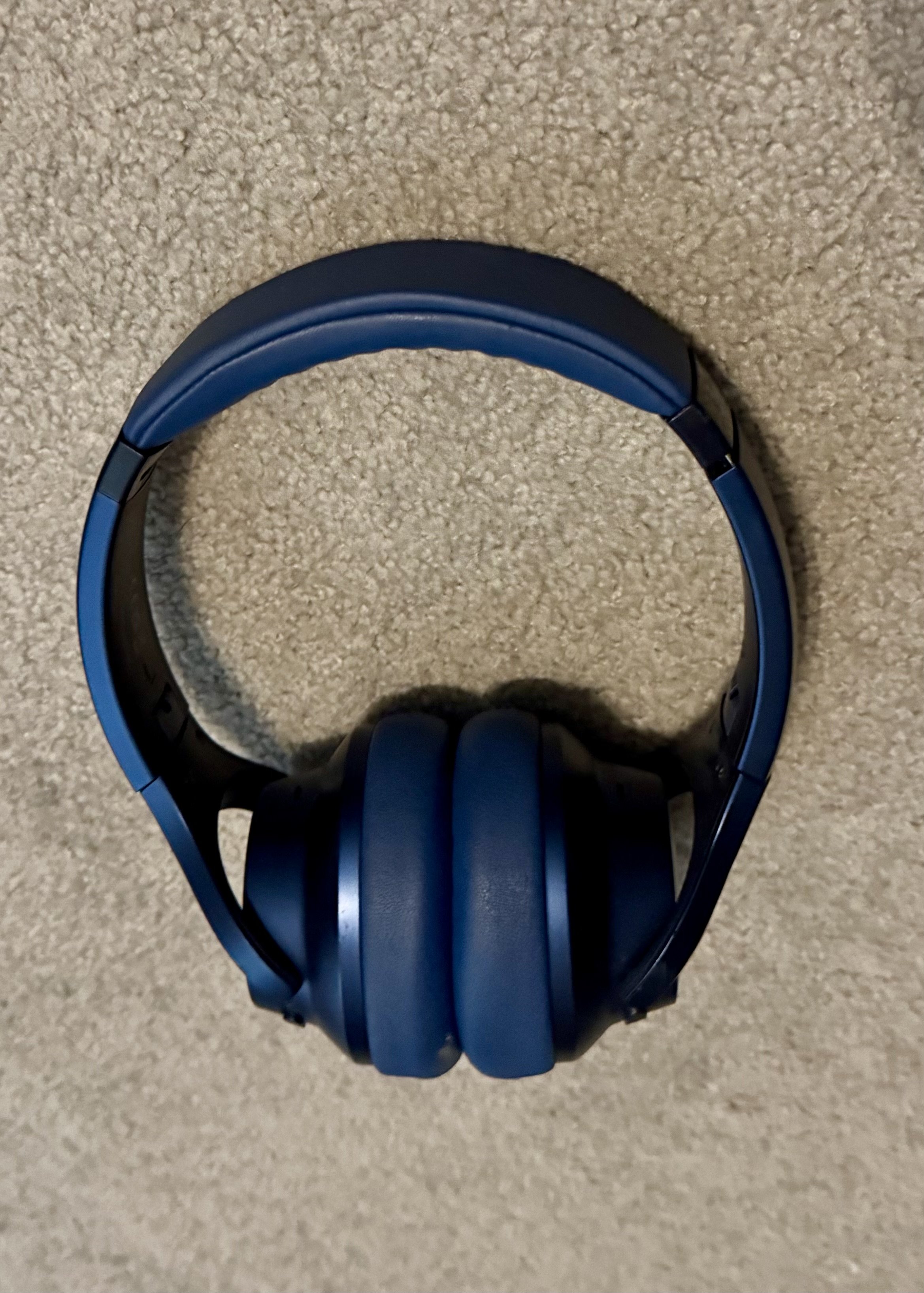 Blue and black over-ear headphones displayed on a textured beige carpet surface.